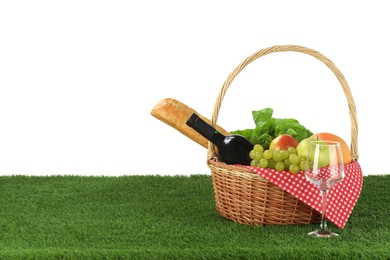 Photo of Picnic wicker basket with food, bottle of wine and glass on grass against white background. Space for text