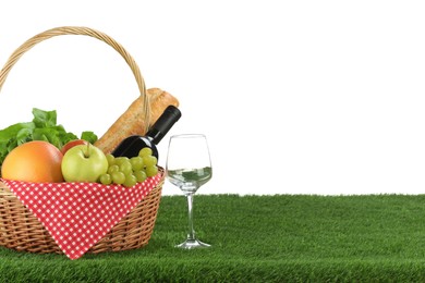 Photo of Picnic wicker basket with food, bottle of wine and glass on grass against white background. Space for text