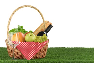 Picnic wicker basket with food, bottle of wine and glass on grass against white background. Space for text