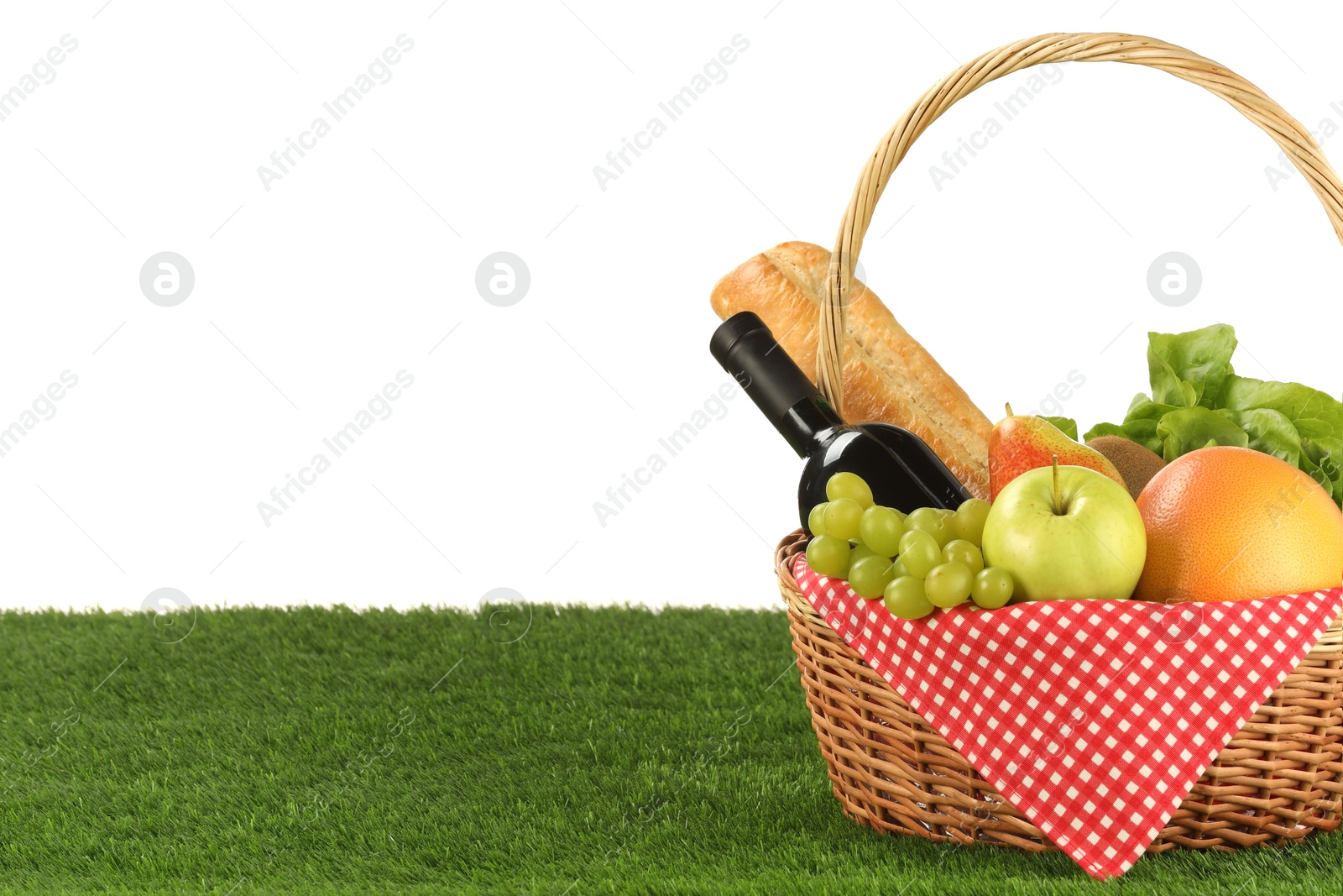 Photo of Picnic wicker basket with food and bottle of wine on grass against white background. Space for text