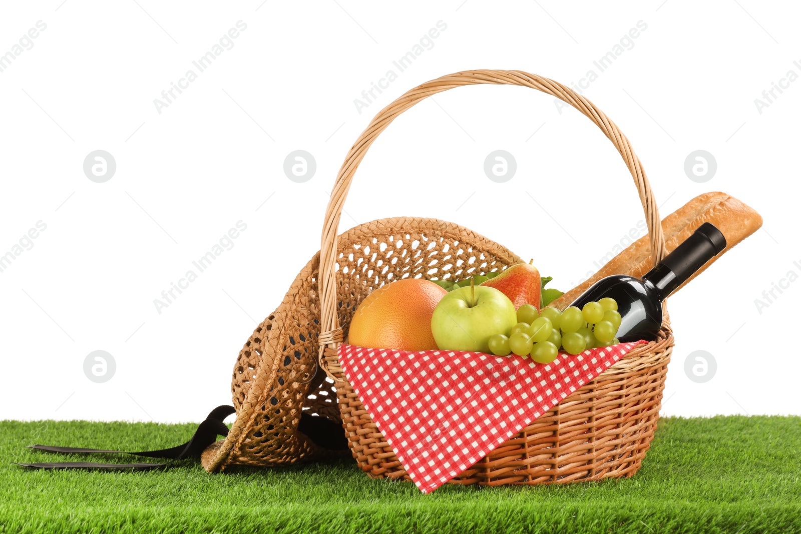 Photo of Picnic wicker basket with food, bottle of wine and hat on grass against white background