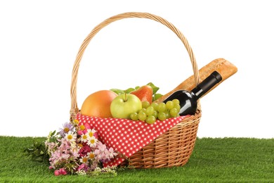 Picnic wicker basket with food, bottle of wine and flowers on grass against white background