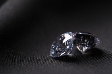 Photo of Two beautiful shiny diamonds on black fabric, closeup. Space for text