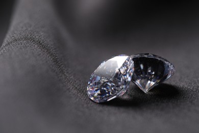 Two beautiful shiny diamonds on black fabric, closeup. Space for text