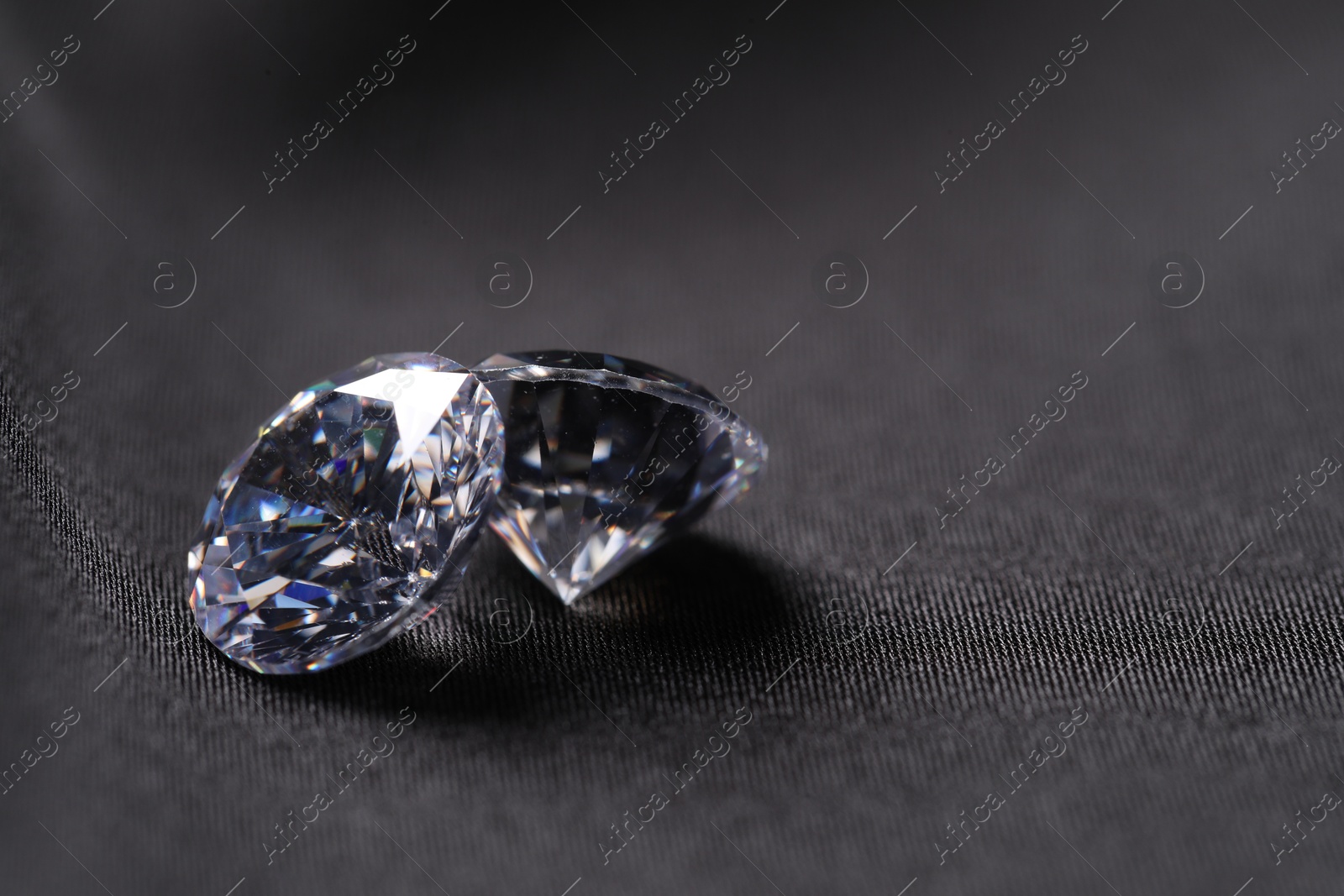 Photo of Two beautiful shiny diamonds on black fabric, closeup. Space for text