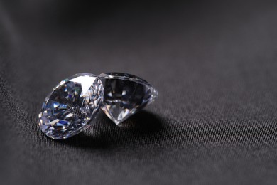 Photo of Two beautiful shiny diamonds on black fabric, closeup. Space for text