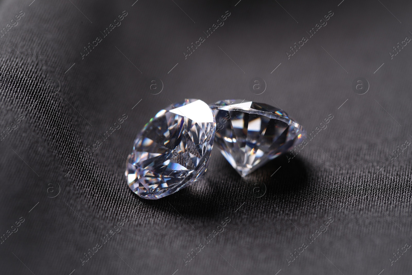 Photo of Two beautiful shiny diamonds on black fabric, closeup