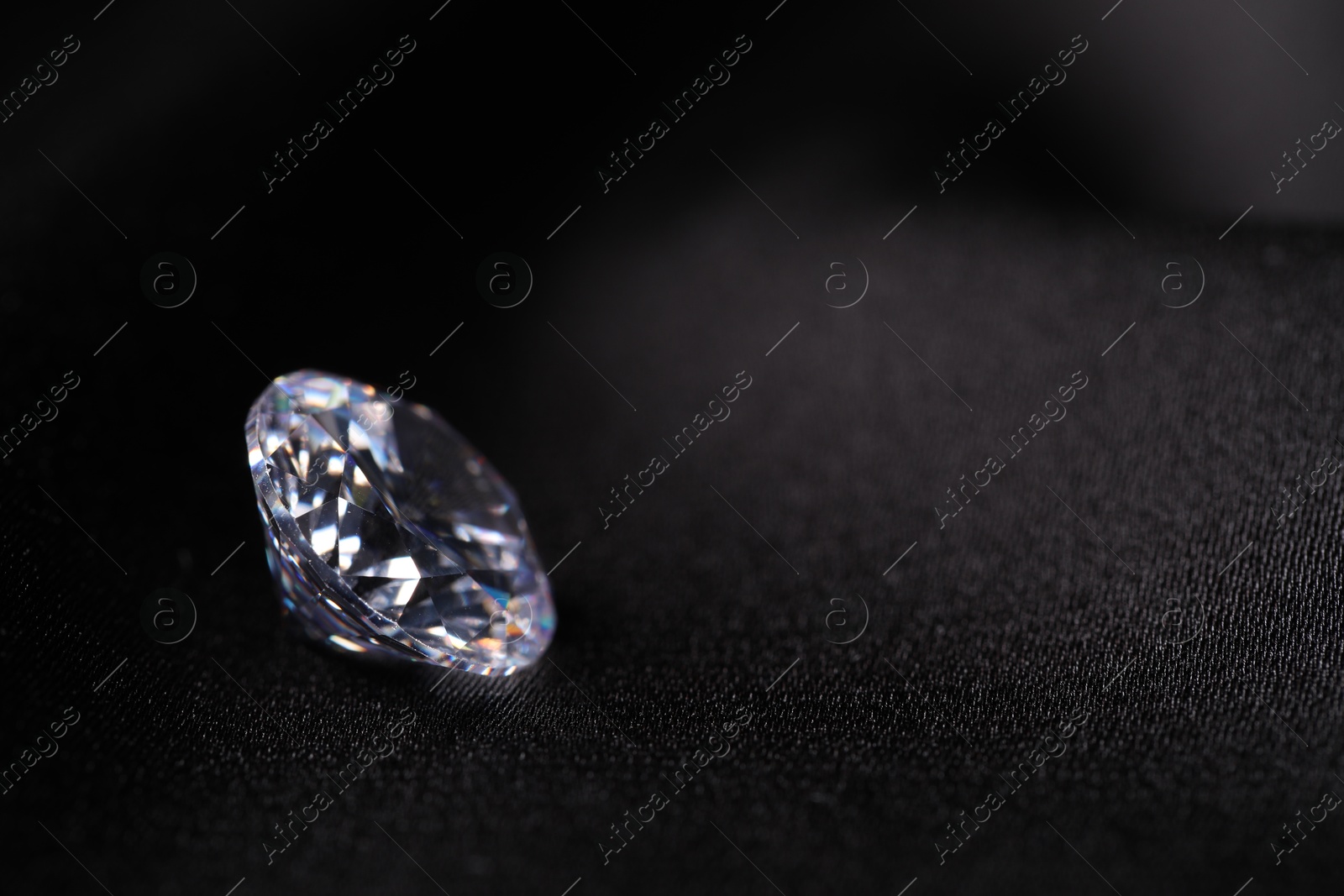 Photo of One beautiful shiny diamond on black fabric, closeup. Space for text