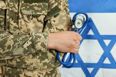 Photo of Man in military uniform with crossed arms and stethoscope against flag of Israel, closeup. Health care concept