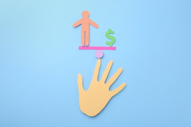 Photo of Equality concept. Paper human figure, dollar sign, seesaw scale and palm on light blue background, top view