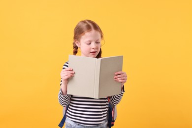 Photo of Cute little girl reading book on yellow background