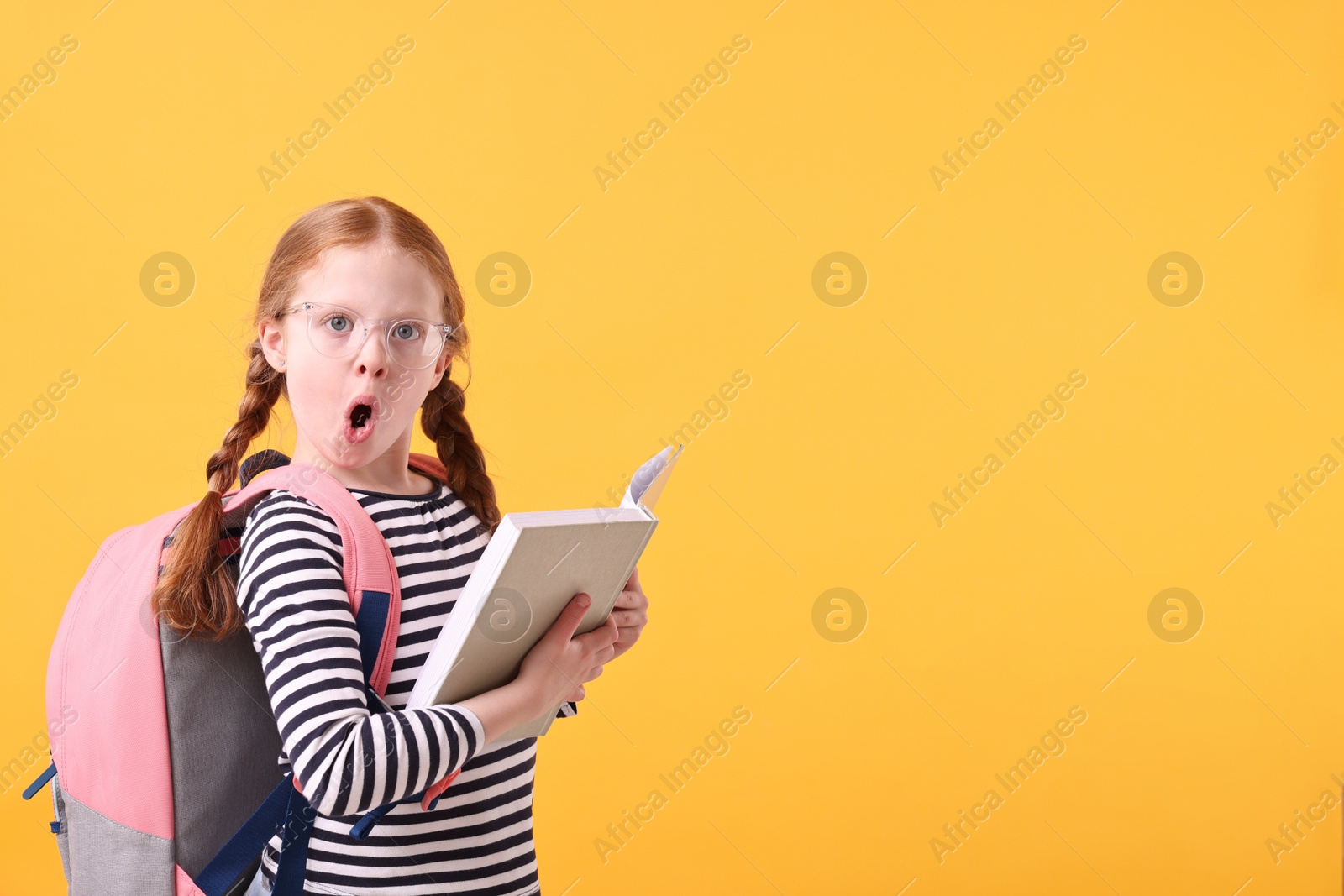 Photo of Surprised girl with book on yellow background. Space for text