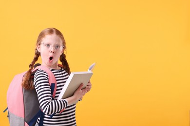 Photo of Surprised girl with book on yellow background. Space for text