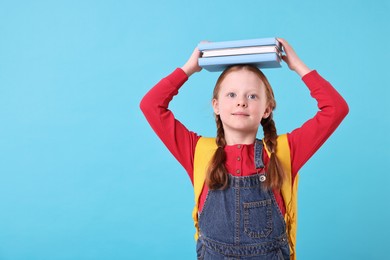 Photo of Cute little girl with stack of books on light blue background. Space for text