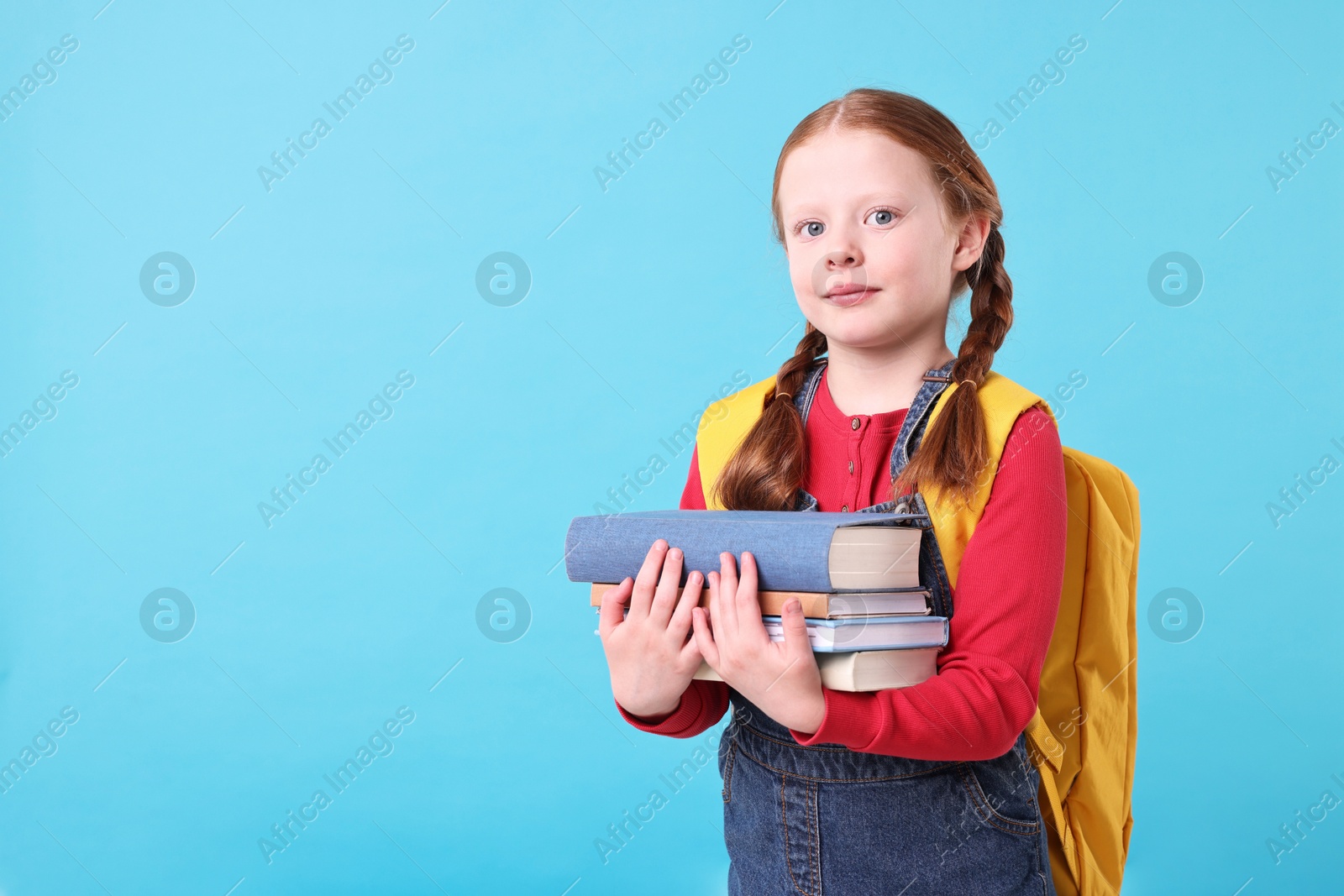 Photo of Cute little girl with stack of books on light blue background. Space for text