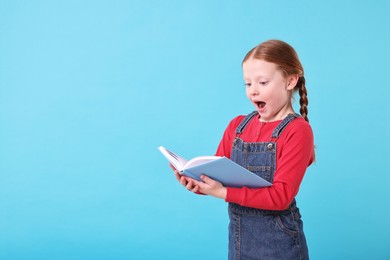 Photo of Surprised girl reading book on light blue background. Space for text