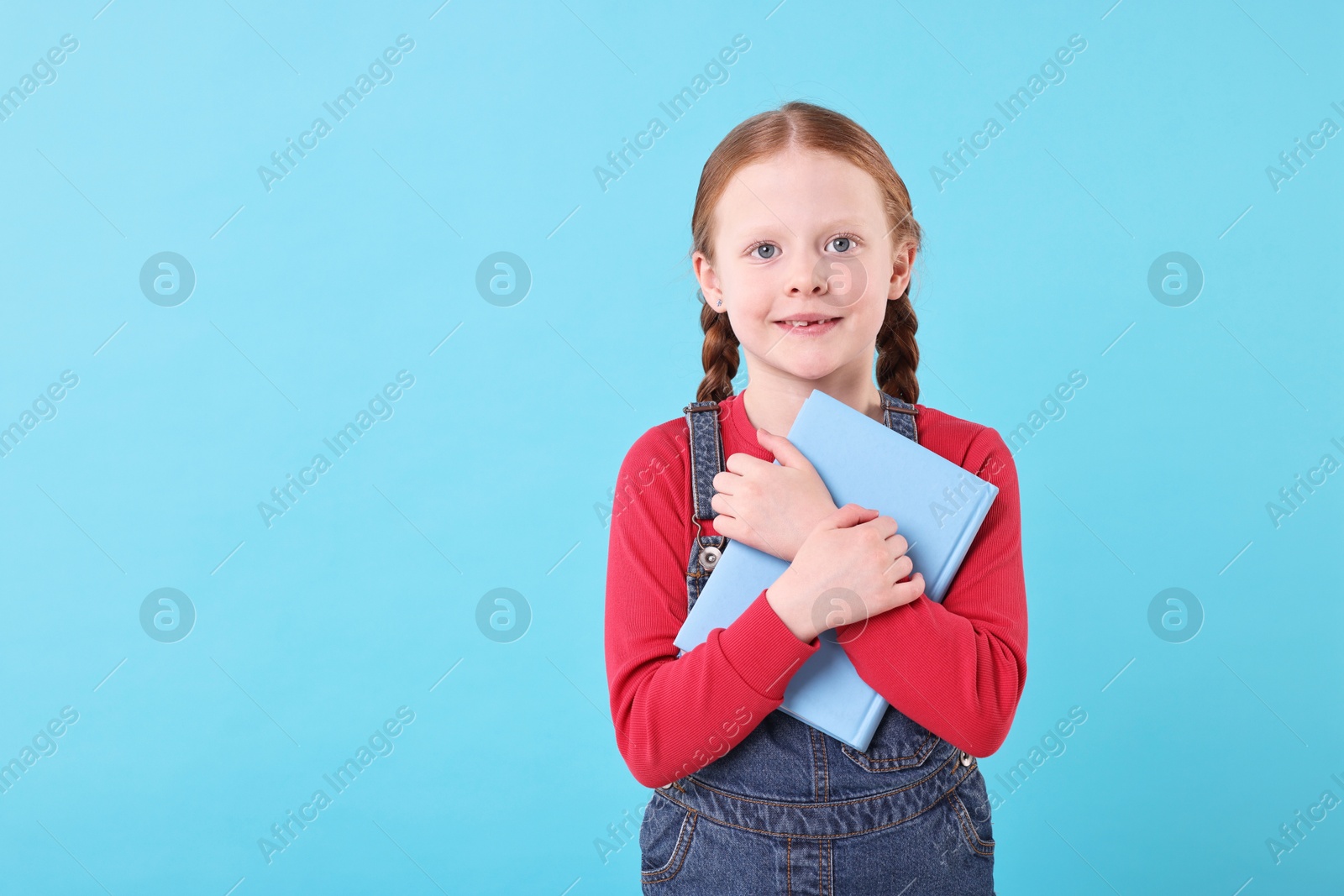 Photo of Smiling girl with book on light blue background. Space for text