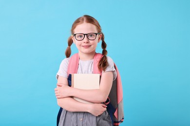 Photo of Cute girl with book and backpack on light blue background