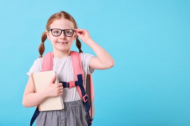 Photo of Smiling girl with book and backpack on light blue background. Space for text