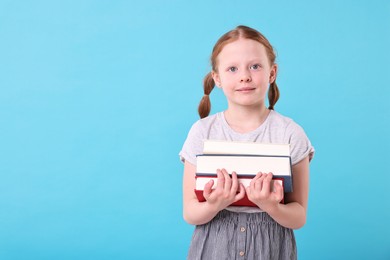 Photo of Cute girl with stack of books on light blue background. Space for text