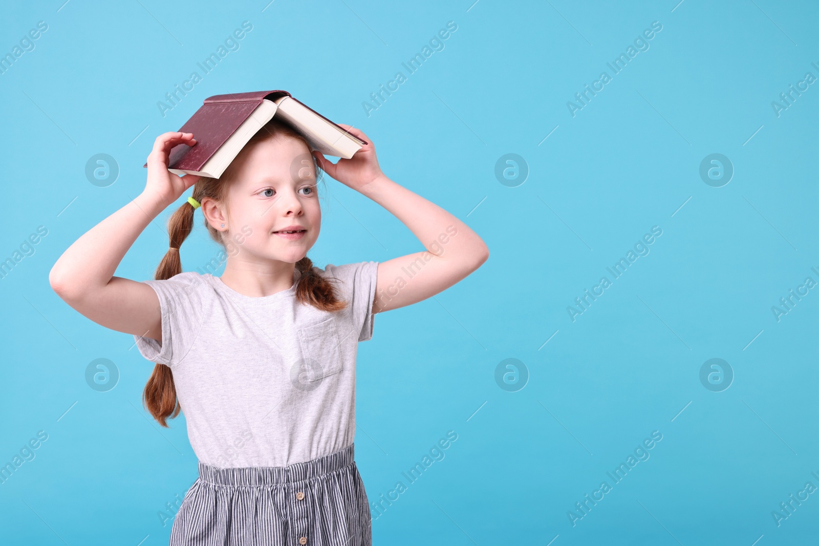 Photo of Cute girl with book on light blue background. Space for text