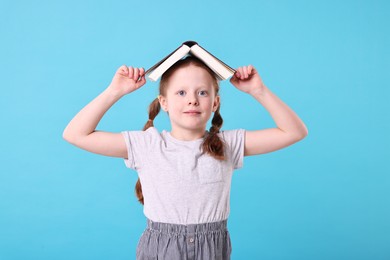 Photo of Cute girl with book on light blue background