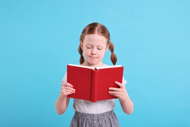 Photo of Cute girl reading book on light blue background