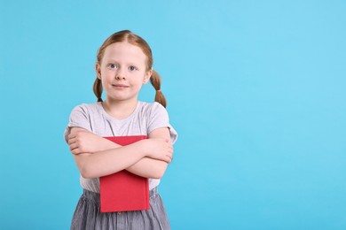 Photo of Cute girl with book on light blue background. Space for text