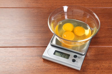 Photo of Kitchen scale with bowl of raw eggs on wooden table. Space for text