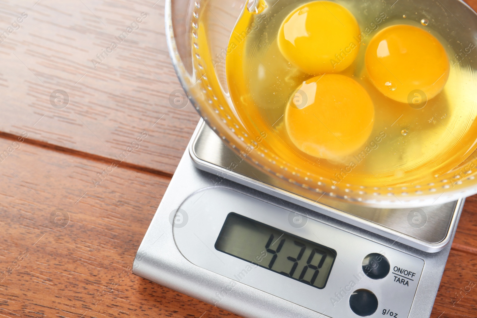 Photo of Kitchen scale with bowl of raw eggs on wooden table, closeup