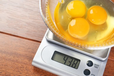 Kitchen scale with bowl of raw eggs on wooden table, closeup