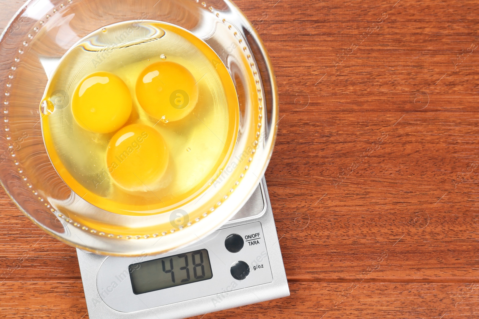 Photo of Kitchen scale with bowl of raw eggs on wooden table, top view. Space for text