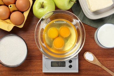 Photo of Flat lay composition of kitchen scale with bowl of raw eggs on wooden table