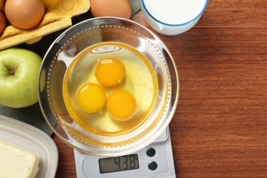 Photo of Flat lay composition of kitchen scale with bowl of raw eggs on wooden table. Space for text