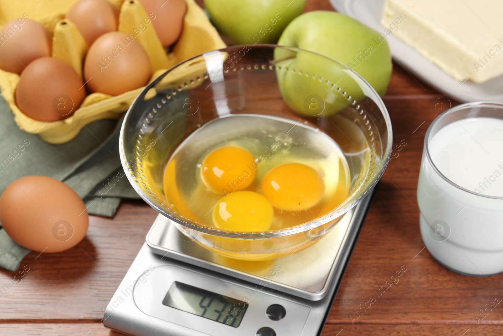 Photo of Kitchen scale with bowl of raw eggs and milk on wooden table, closeup