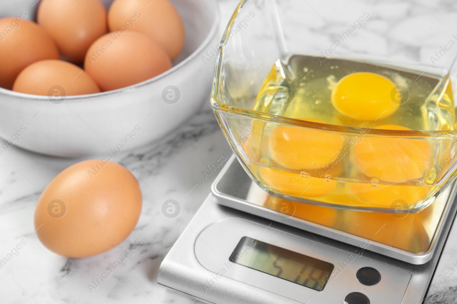 Photo of Kitchen scale with bowl of raw eggs on white marble table, closeup