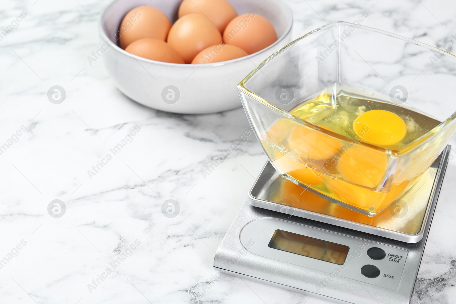 Photo of Kitchen scale with bowl of raw eggs on white marble table, closeup. Space for text