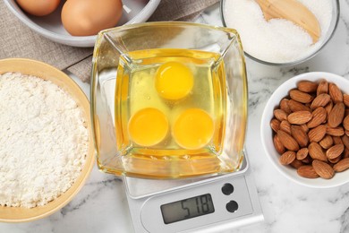 Photo of Flat lay composition of kitchen scale with bowl of raw eggs on white marble table