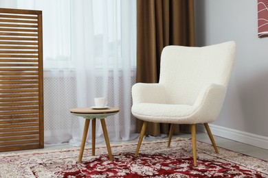 Soft armchair, coffee table and window with curtains in room. Interior design