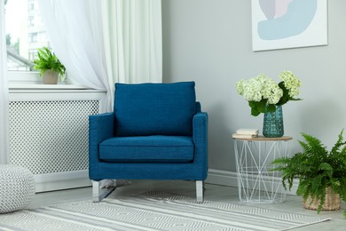 Photo of Soft armchair, side table, flowers and window with curtains in room. Interior design