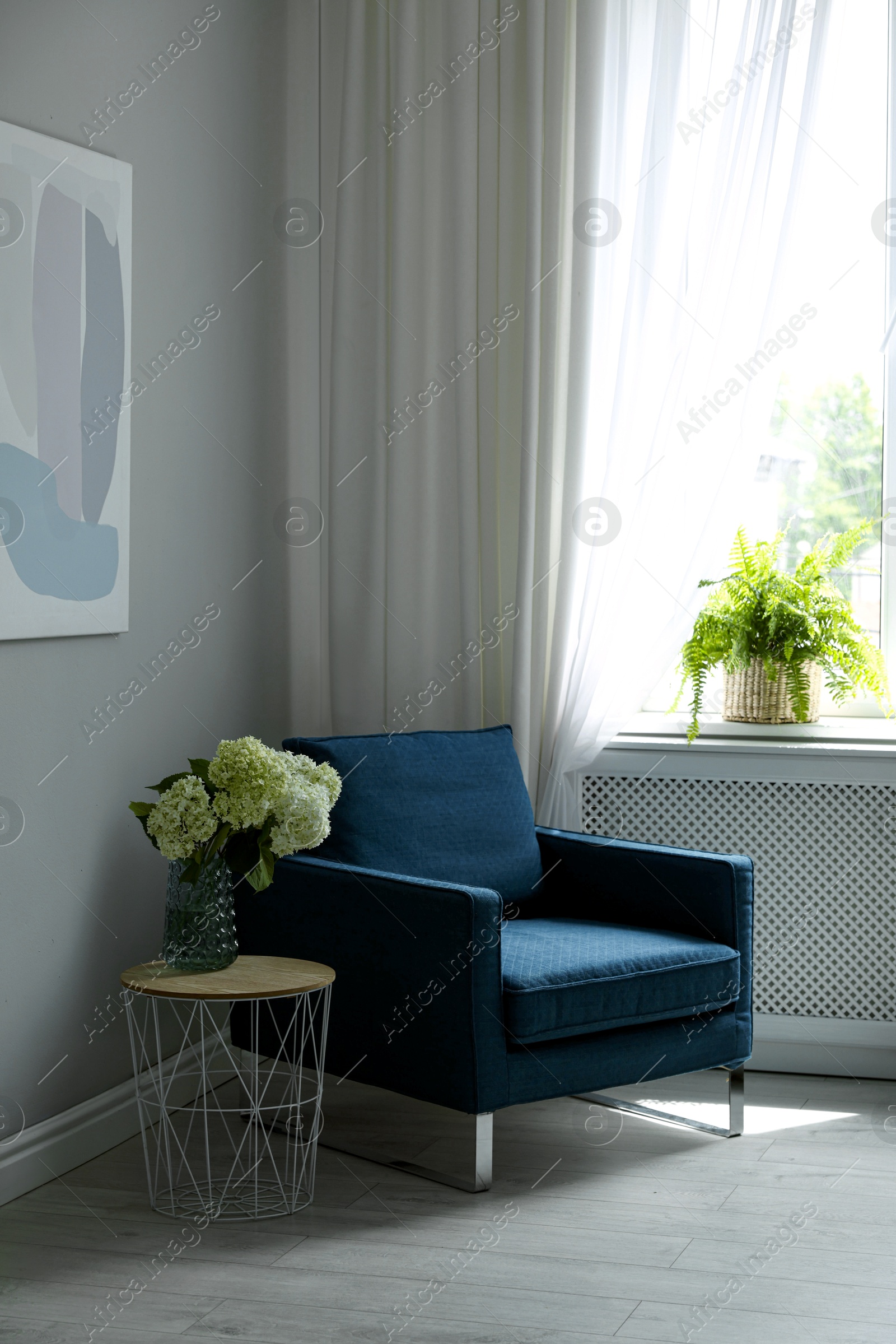 Photo of Soft armchair, side table, flowers and window with curtains in room. Interior design