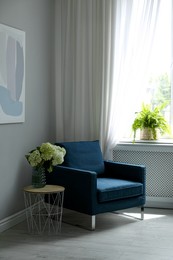 Photo of Soft armchair, side table, flowers and window with curtains in room. Interior design