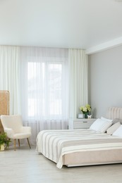 Photo of Large bed, chest of drawers, armchair and window with curtains in bedroom. Interior design