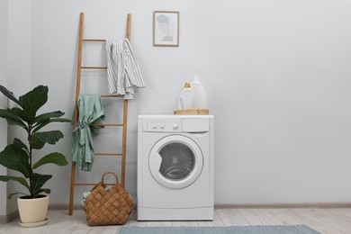 Photo of Washing machine, detergents, houseplant and ladder in laundry room, space for text