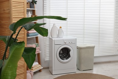 Photo of Washing machine, detergents, towels and basket in laundry room