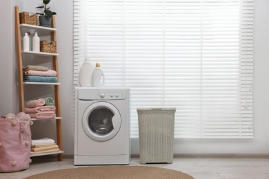 Photo of Washing machine, detergents, towels and basket in laundry room