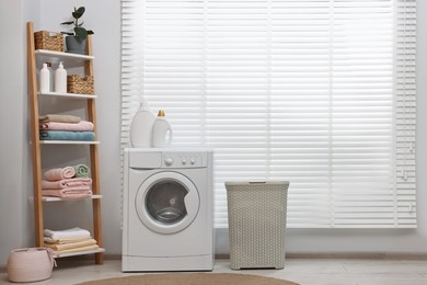 Photo of Washing machine, detergents, towels and basket in laundry room