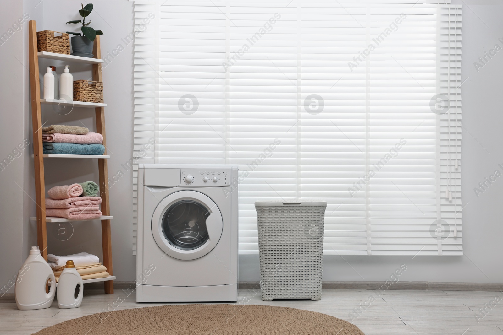 Photo of Washing machine, detergents, towels and basket in laundry room