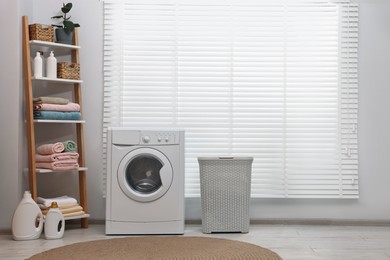 Photo of Washing machine, detergents, towels and basket in laundry room