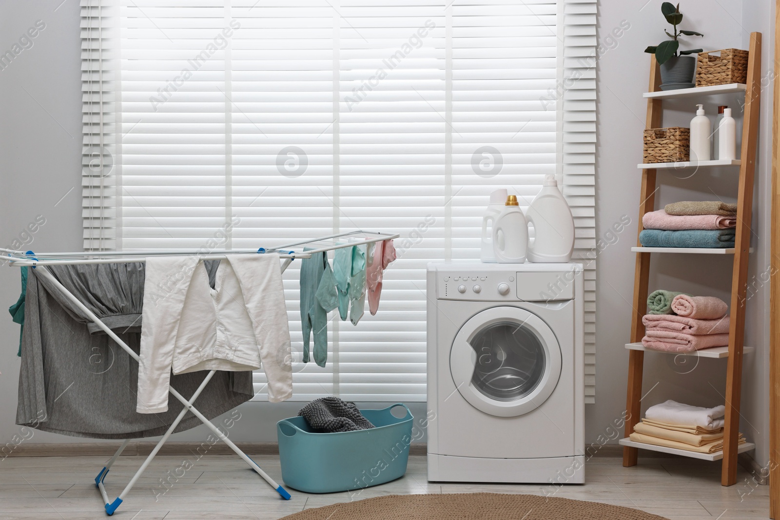 Photo of Washing machine, detergents, towels, basket and drying rack in laundry room